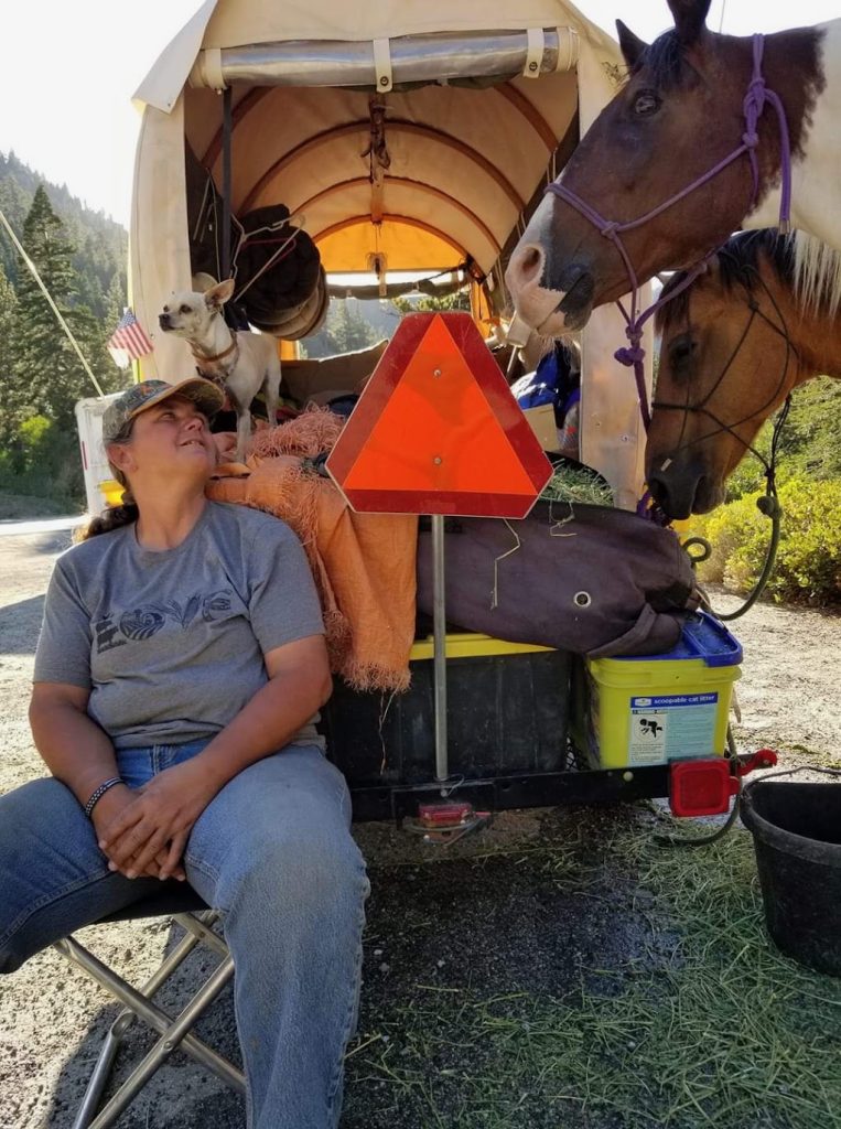 Angela Wood resting by her covered wagon with her dog Shotzi and horses Renegade and Starbuck